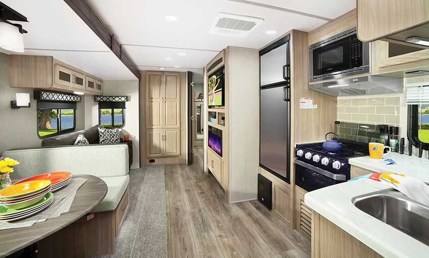 Kitchen and dinette of Coachmen Freedom Express 326BHDS Liberty Edition Kitchen in travel trailer with stainless steel double-door refrigerator and white countertops across from dinette.