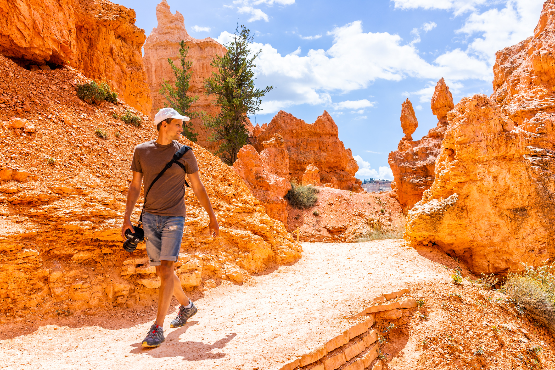Man tourist person walking motion by orange color formations at Queens Garden Navajo Loop trail at Bryce Canyon National Park in Utah with camera