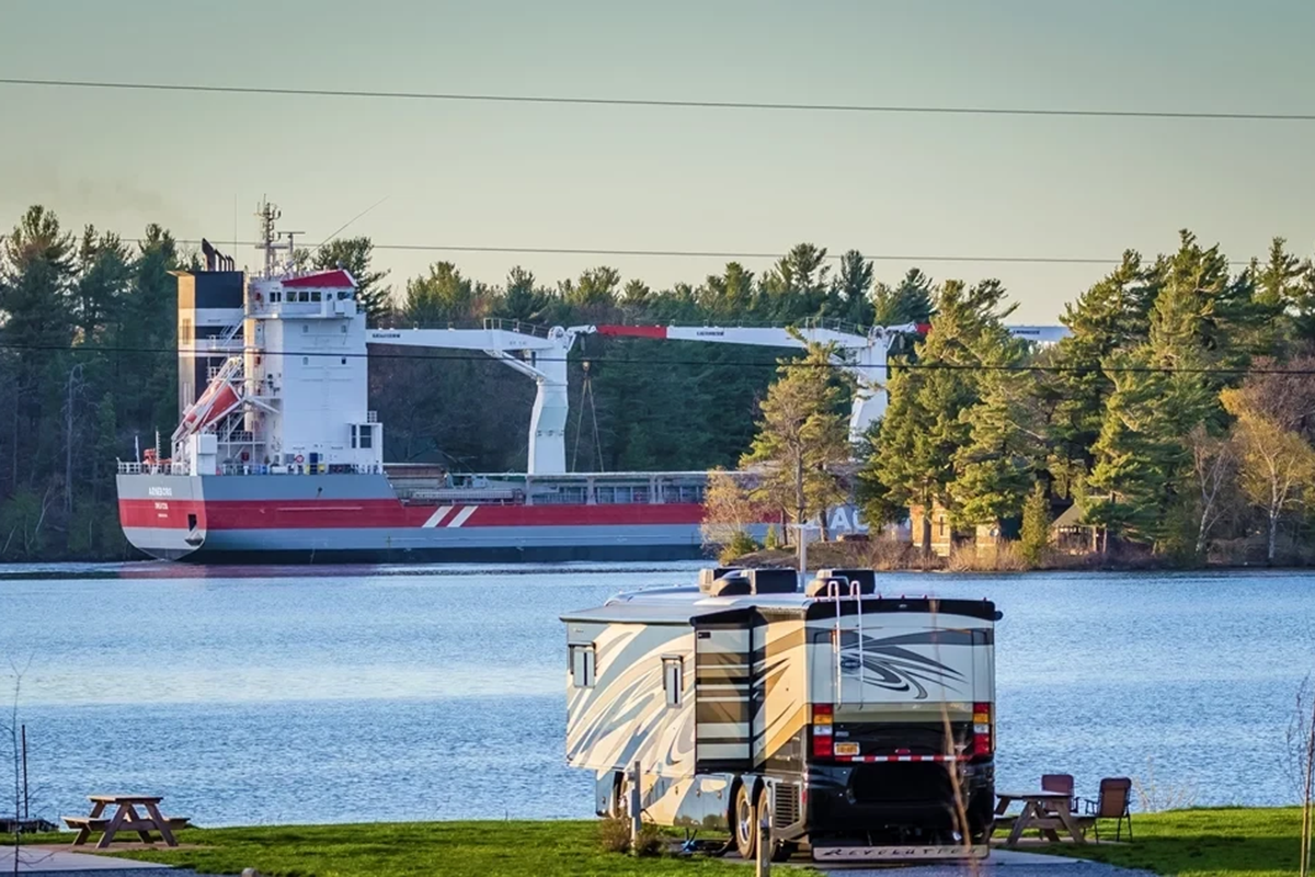 An RV on its spot in foreground, with river-going commercial vessel in background. 