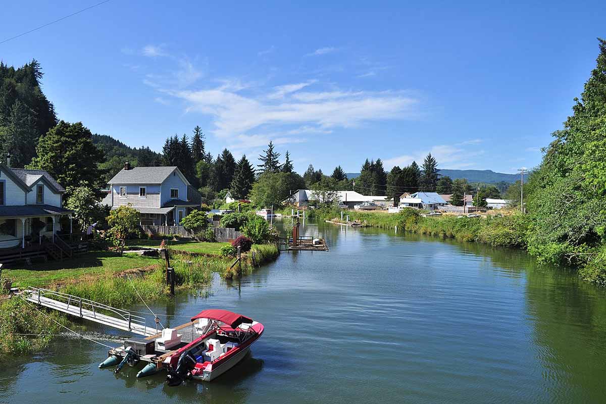 A creek with quaint houses and lush trees and grass on each bank.