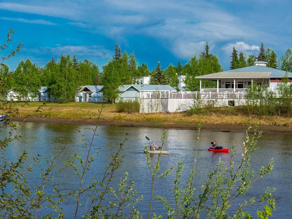 Two kayakers paddle near a woodsy bank.