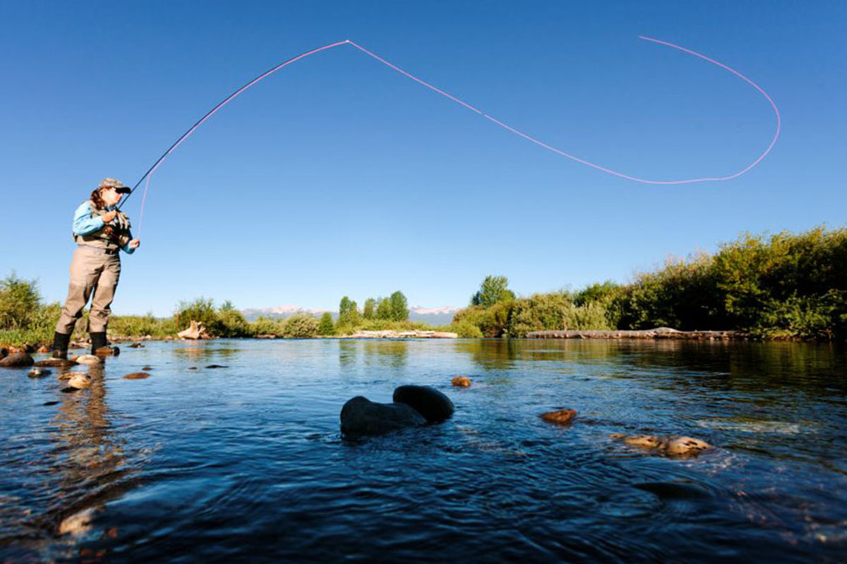 A woman casts a long line on a slow-moving river.